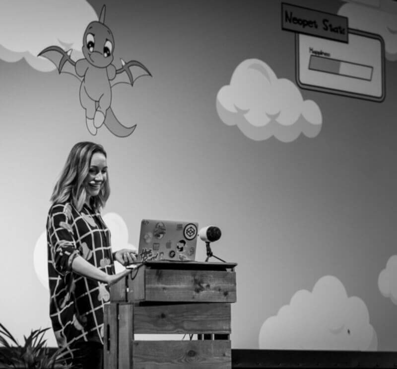 black and white photo of Cassie on stage at beyond tellerrand. Screen behind her shows an SVG neopet.